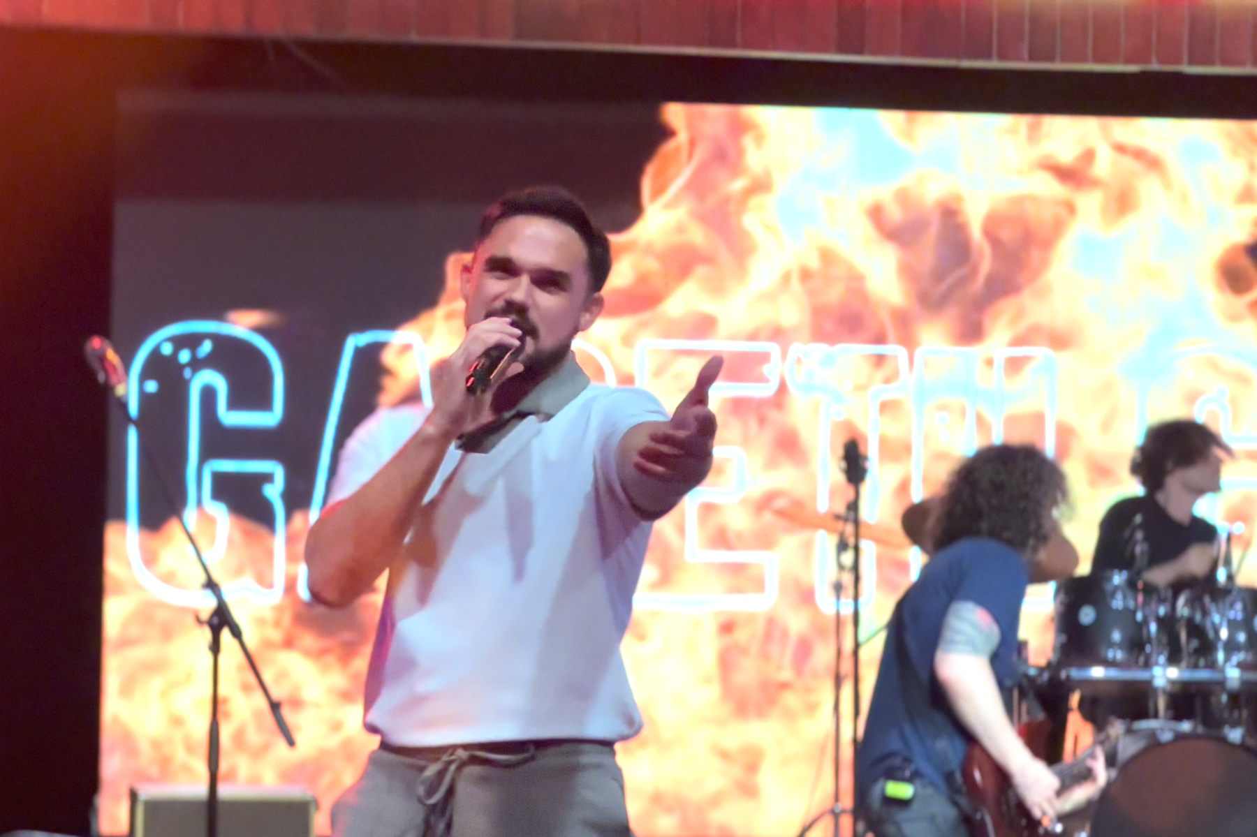 Gareth Gates on stage in front of a flaming screen reaching out to an audience member