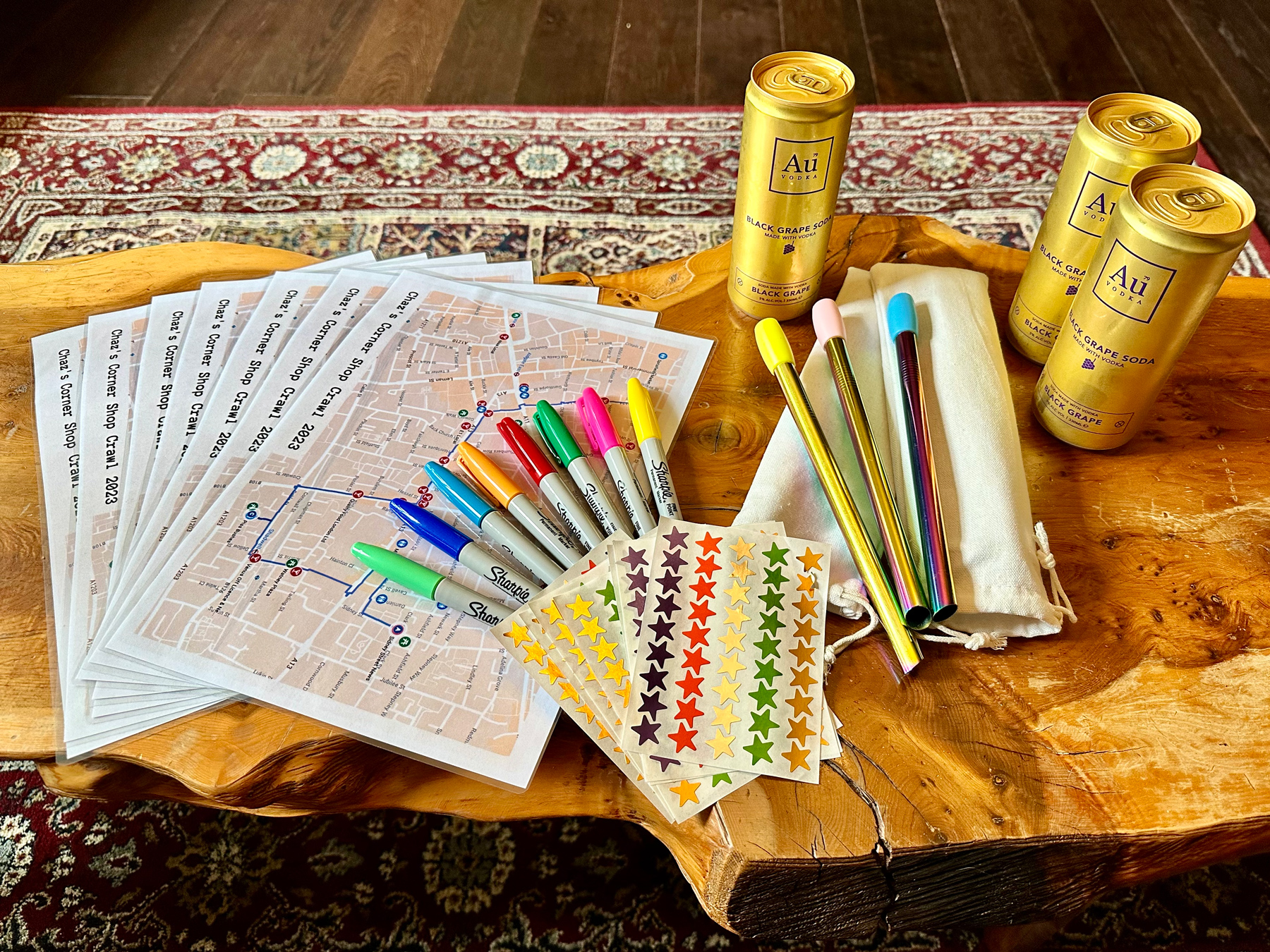 A selection of maps, Sharpies, star stickers, reusable straws, and cans of AU Black Grape Soda laid out on a table ready for our corner shop crawl
