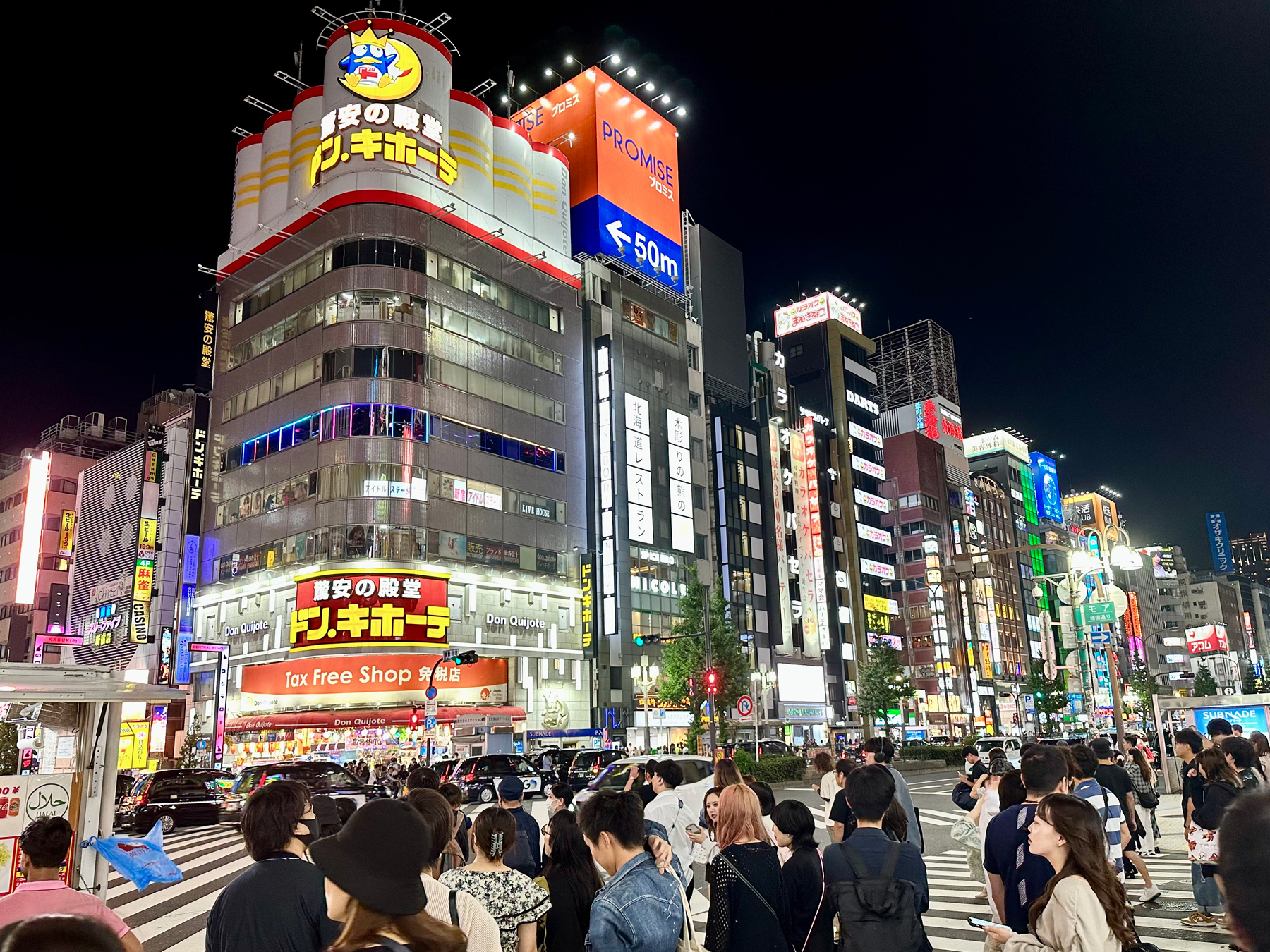 A view across a busy street crossing in Kabukicho, to tall buildings covered in lit-up signs