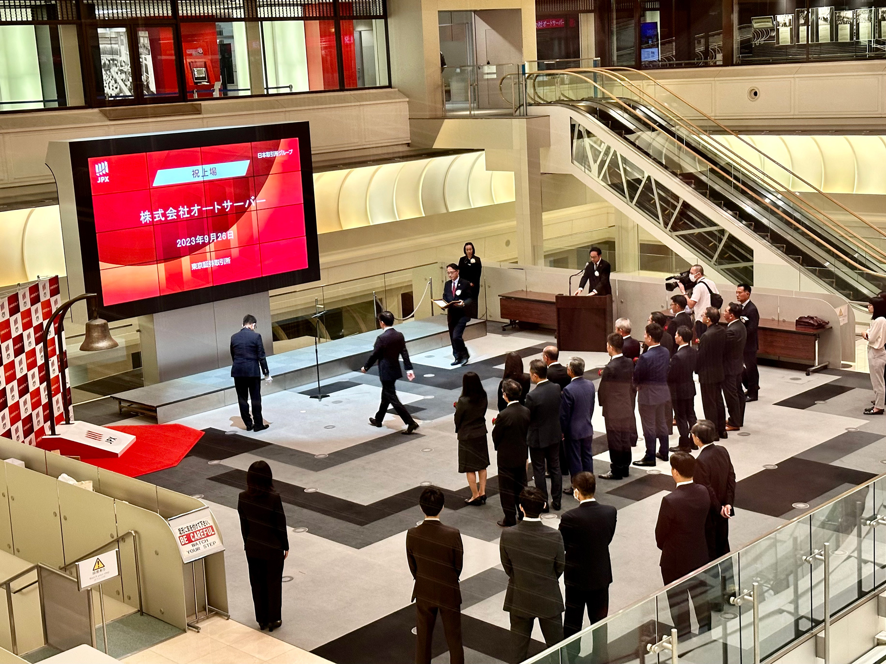 A group of suited people standing in front of the stock exchange screen, their company being added to the stock exchange
