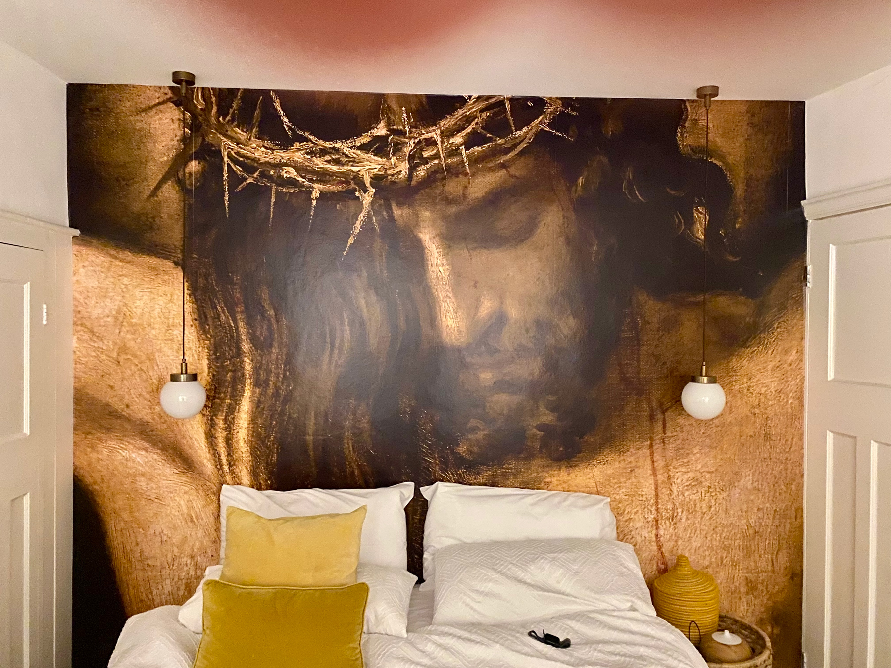 A full-wall mural of a crucified Jesus in a crown of thorns, looking down on a double bed