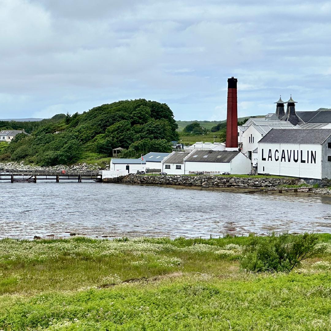 A view of the Lagavulin distillery from the coast, white brick buildings with a painted black sign and a bright red chimney