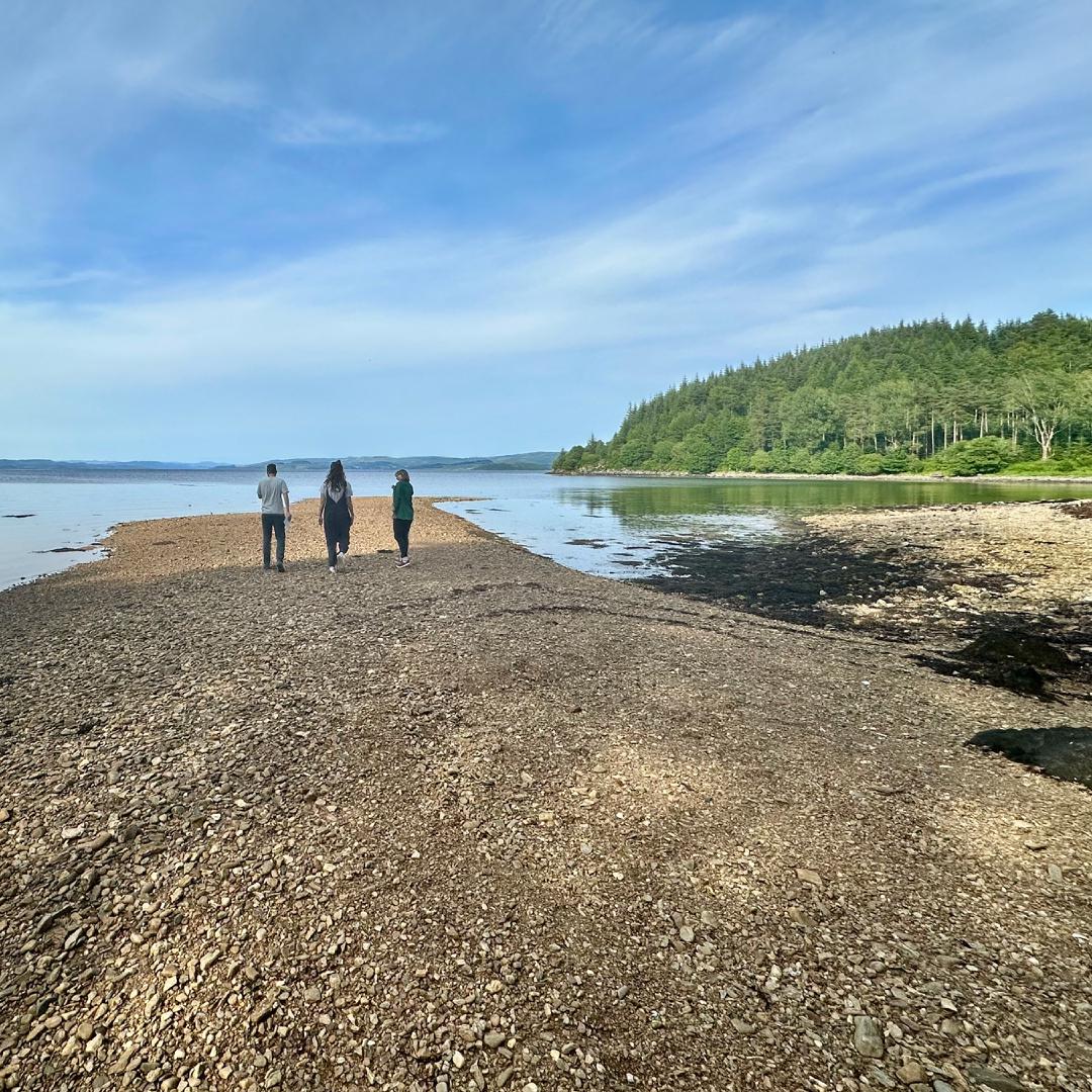 Charlotte, her brother, and his girlfriend looking out over a clear loch on a sunny day