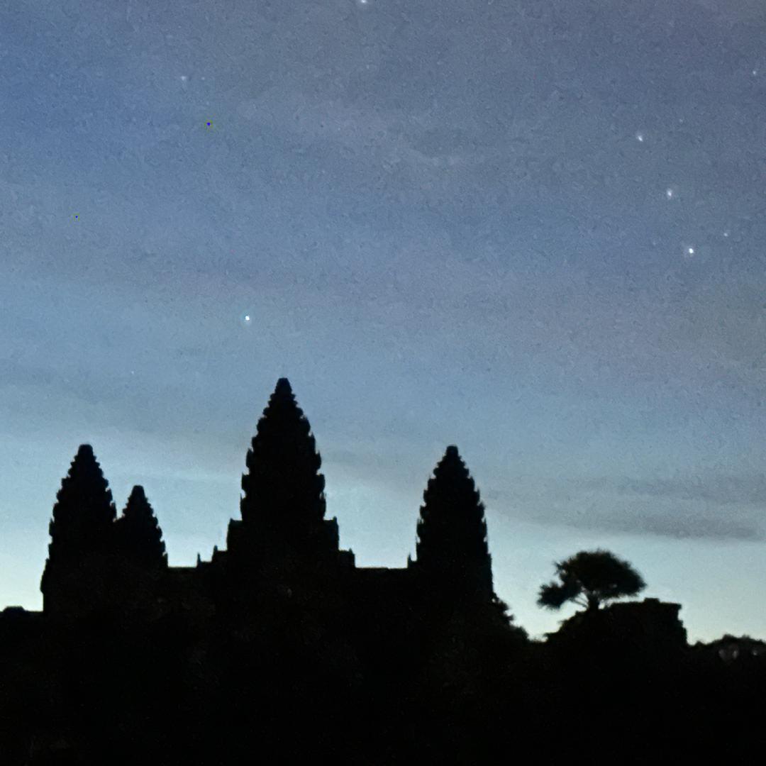 A silhouette of Angkor Wat against the night sky, a large temple with multiple spires