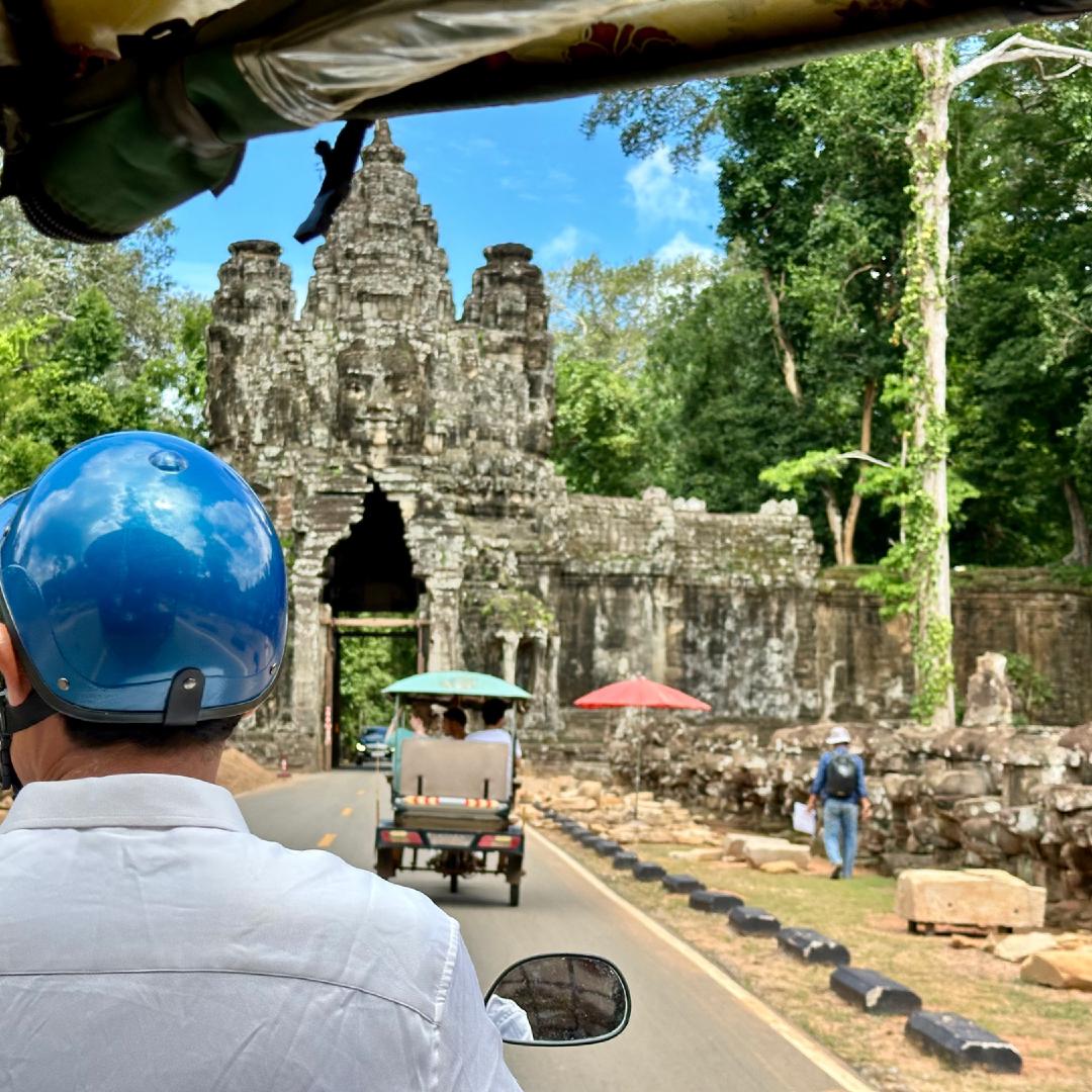 The view from a Tuk Tuk. Another Tuk Tuk is in front and about to drive through a gate in an intricate temple wall