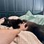 A cute black cat laying on a bed, looking at the camera. He's exposing his belly which is being rubbed.