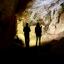 Two silhouettes deep in a cave, both using their phone torches to light the way
