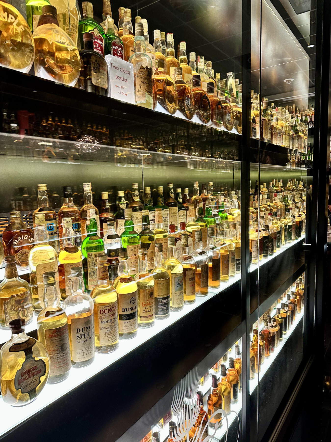 A large glass cabinet packed full of old bottles of whisky
