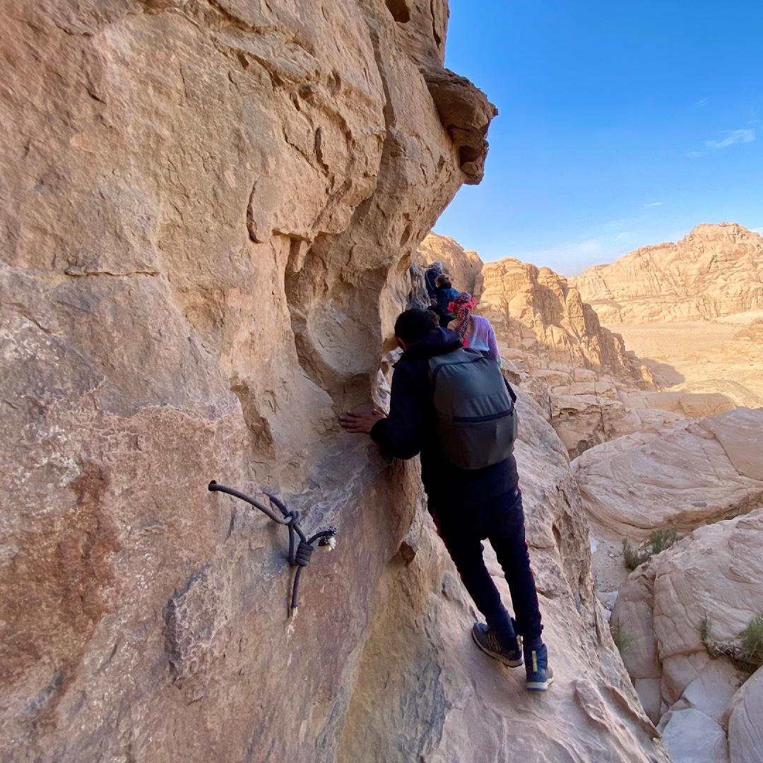 A row of people climbing along a narrow ridge in a desert mountain