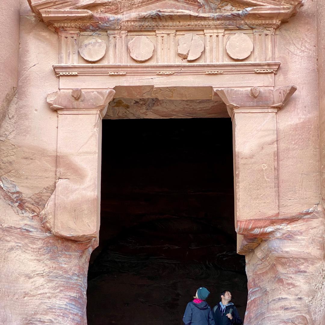 Two people standing in the massive entrance of a tomb